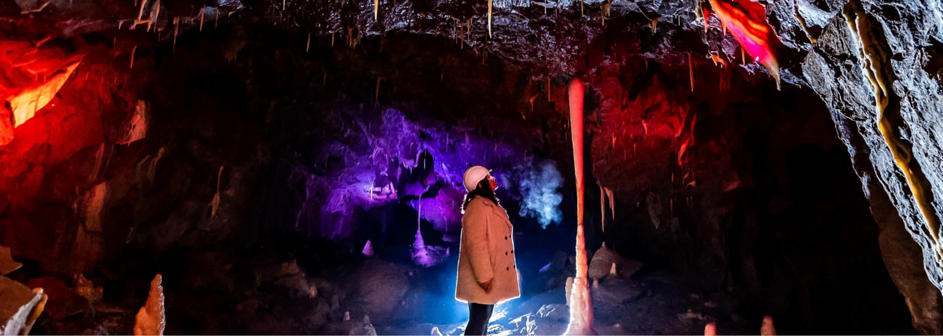 A person stands in a cave illuminated by colorful lights.