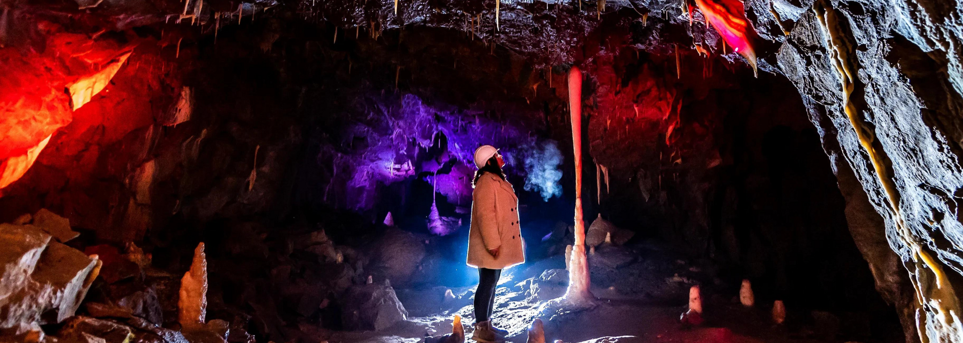 Person in a cave lit by red, purple, and blue lights, looking upward.