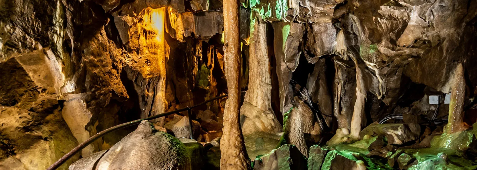 Cave interior with stalactites and stalagmites, illuminated by warm light.