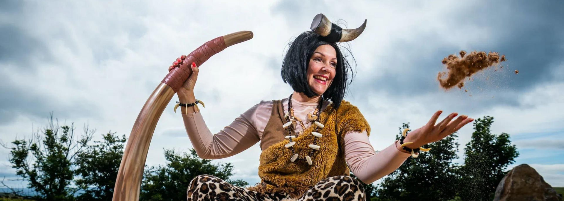 A person wearing a costume with horns throws dirt in the air, smiling.