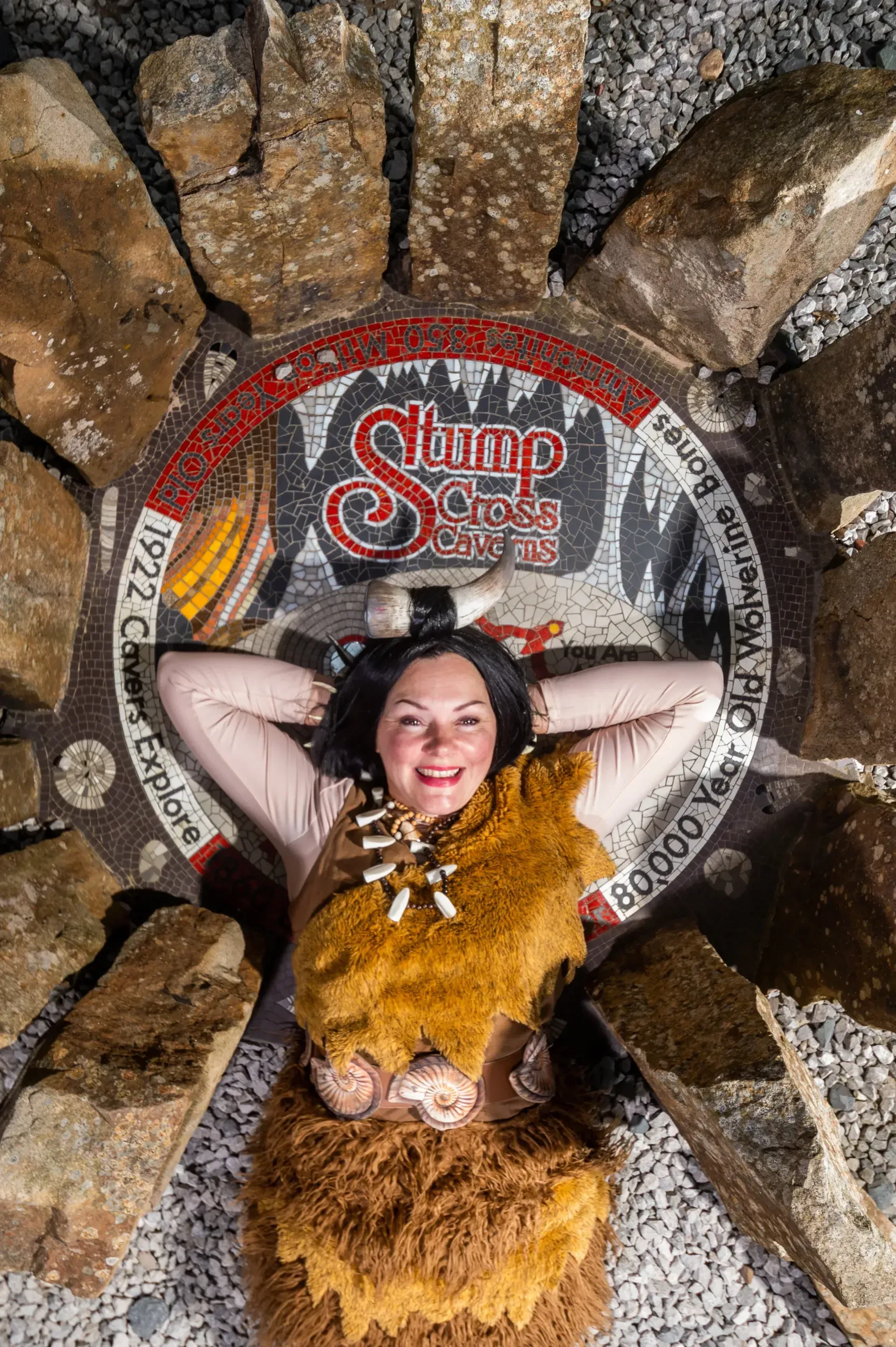 Woman lying on a Stump City sign, surrounded by rocks. She is wearing a brown outfit and smiling.