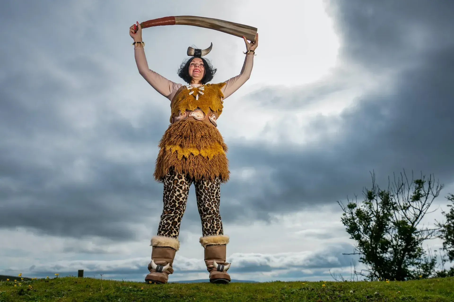 Woman in Viking costume holding a sword aloft, against a cloudy sky.