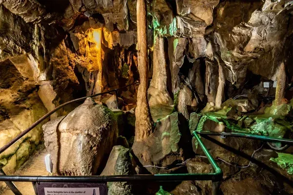 Rocky cave interior with illuminated stalactites and a rope walkway over green-lit water