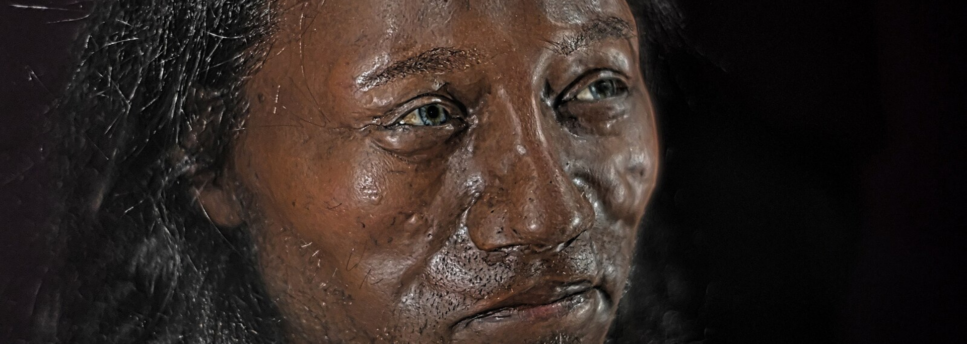 Close-up of a person's face; brown skin, dark hair, eyes focused with a slightly somber expression.