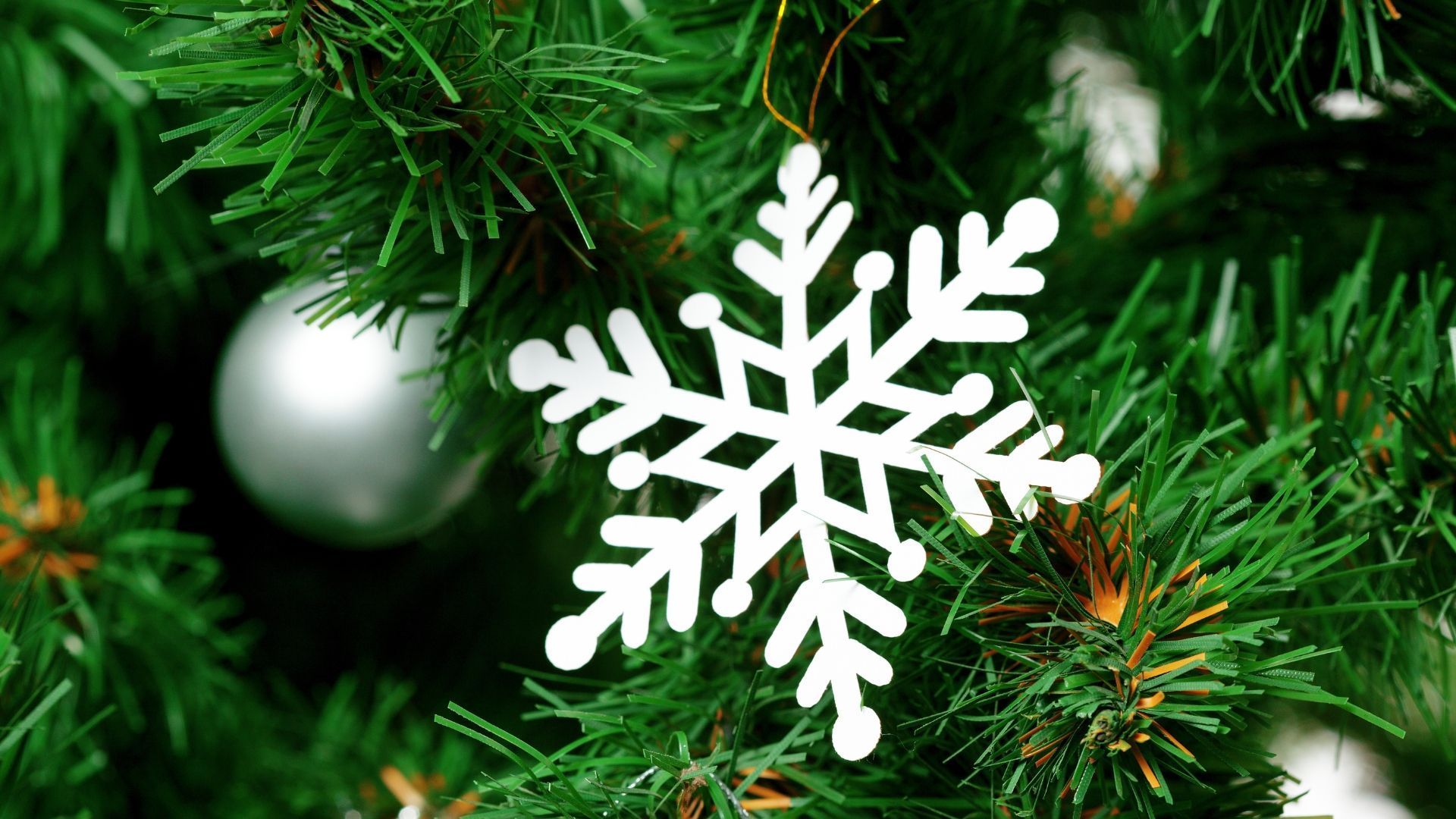 White snowflake ornament hanging on a Christmas tree with silver ball.