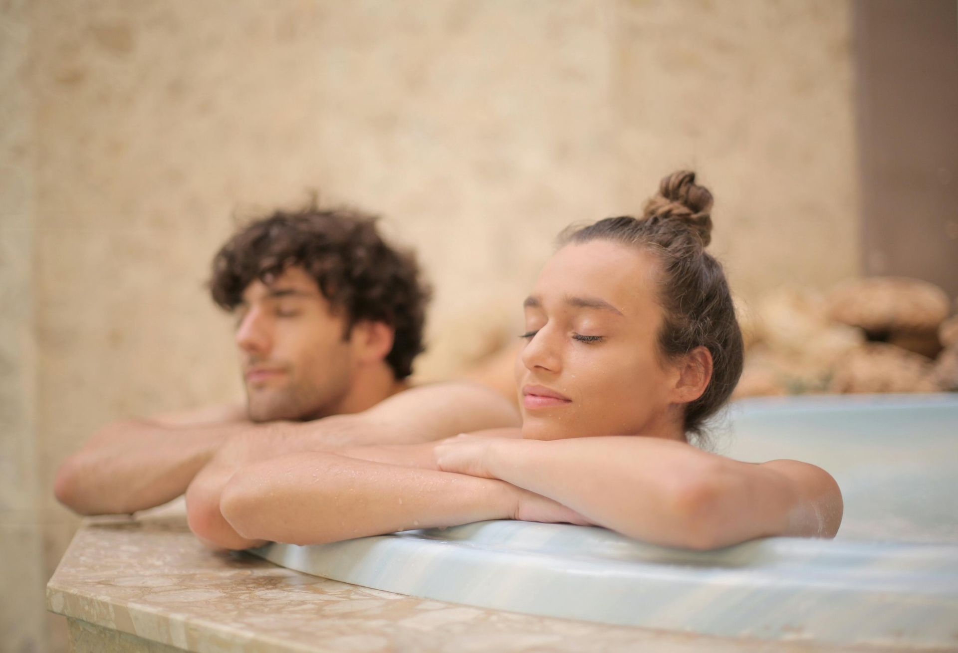 Man and woman relaxing in a spa, leaning on the edge with eyes closed.