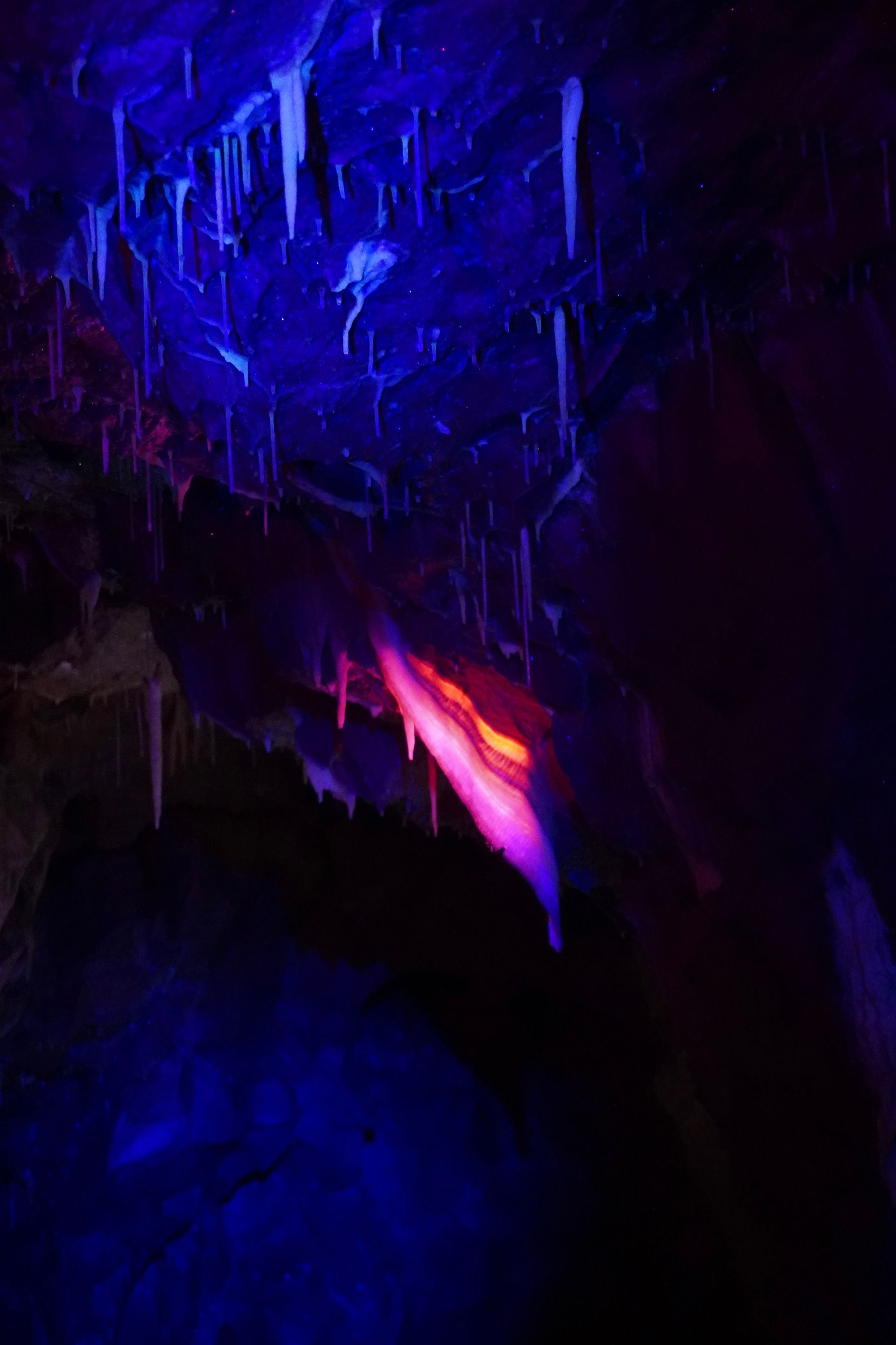 Red-lit cave with a bright pink stalactite-like formation and purple light reflecting on the floor