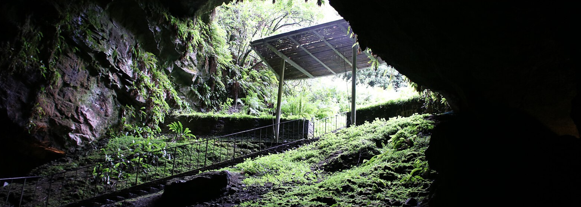 View from a dark cave opening towards a shelter, lit by outside sunlight.