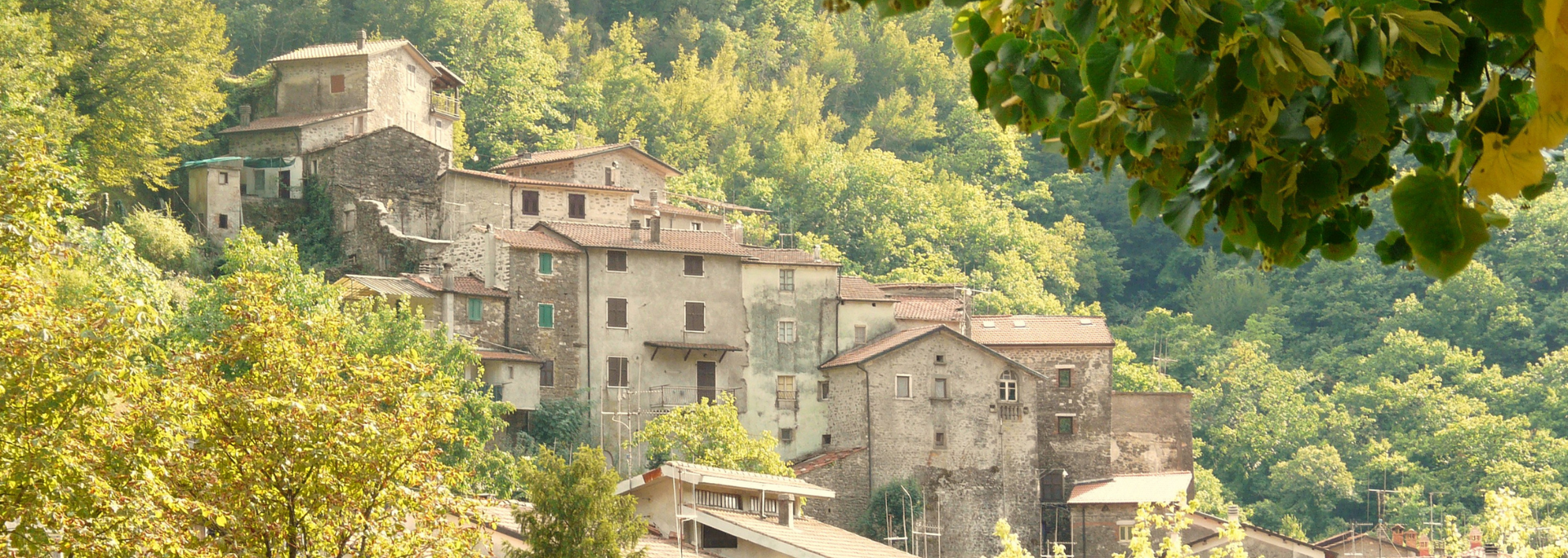 Old stone buildings nestled among trees on a hillside.