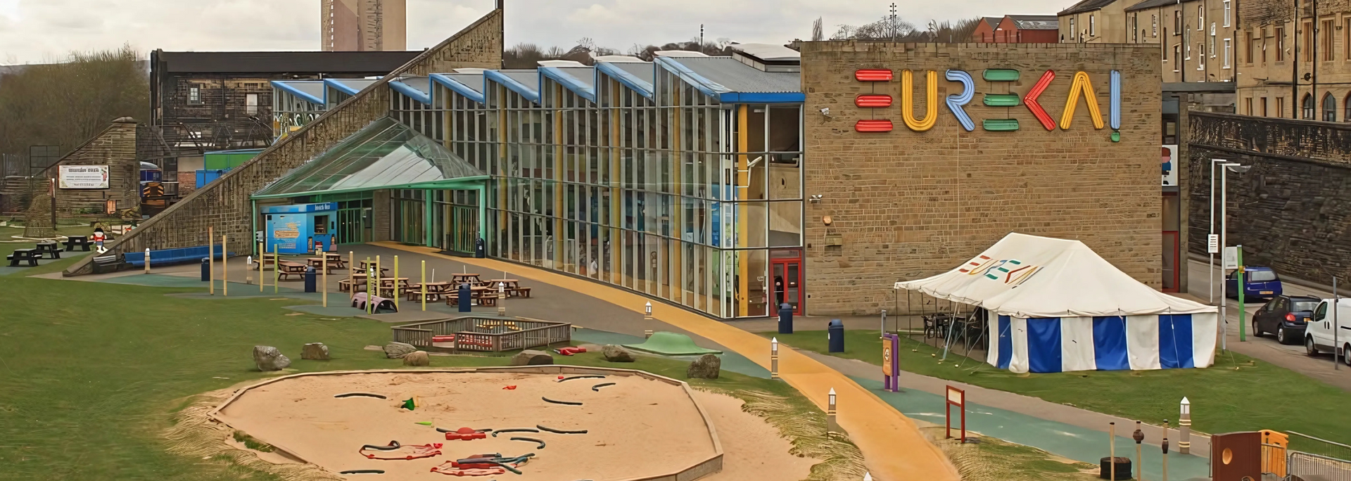 Eureka! The building exterior with colorful signage, featuring a tent, a playground and grassy areas.