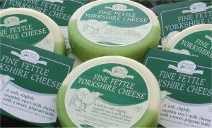 Green-waxed Fine Fettle Yorkshire cheese wheels, stacked with labels.