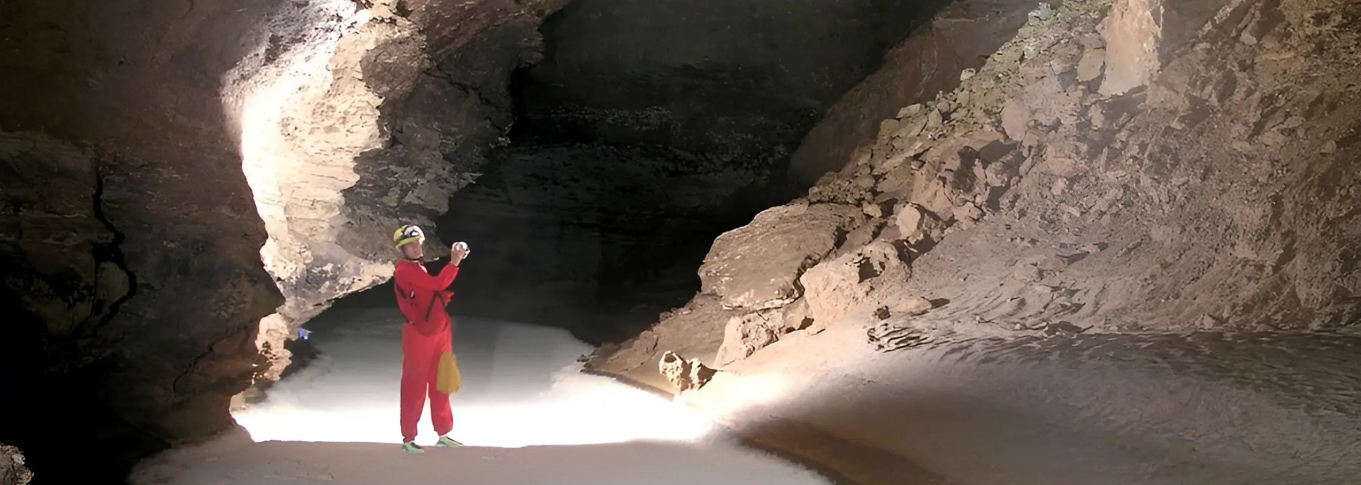 Person in red suit explores a cave, illuminated by a light source.