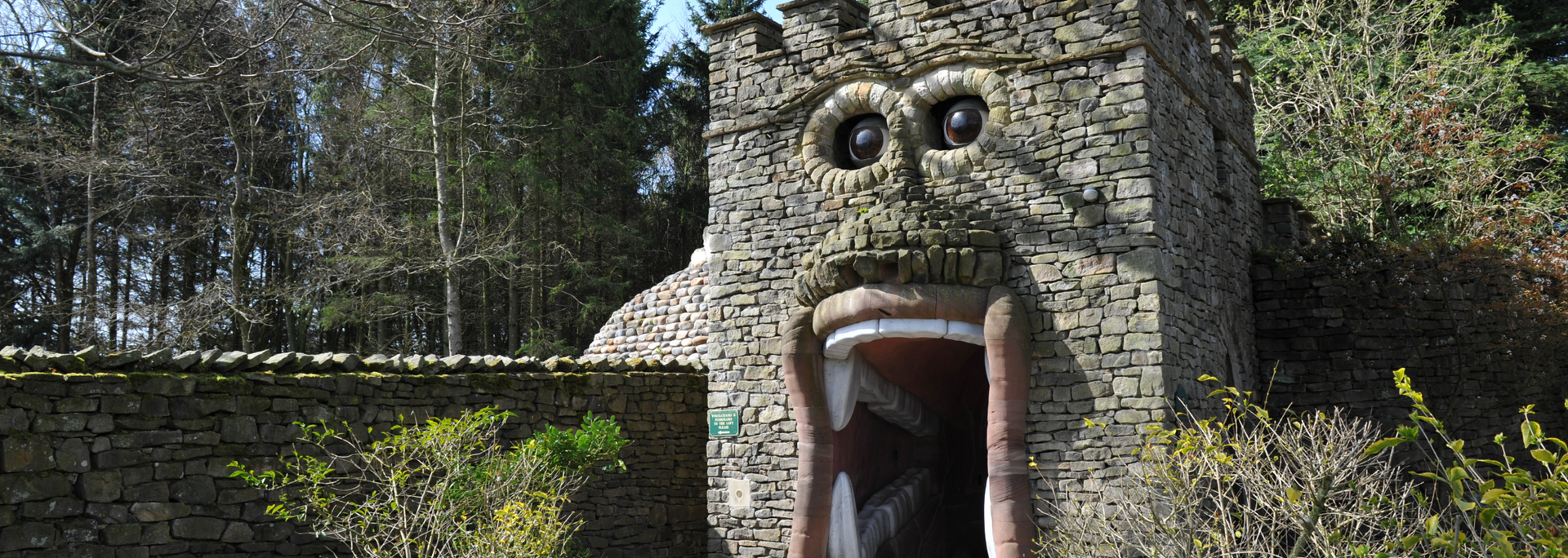 Stone structure with a large open mouth and eyes, resembling a monster. Trees and greenery in the background.