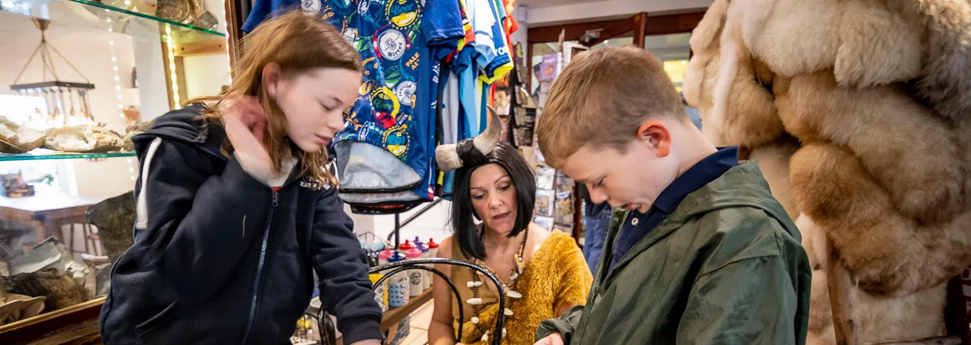 Three people looking at something in a shop, with clothes and objects around.