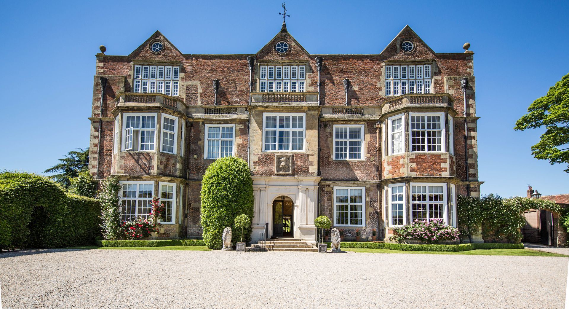 Large brick mansion with multiple windows, set in a gravel driveway on a sunny day.