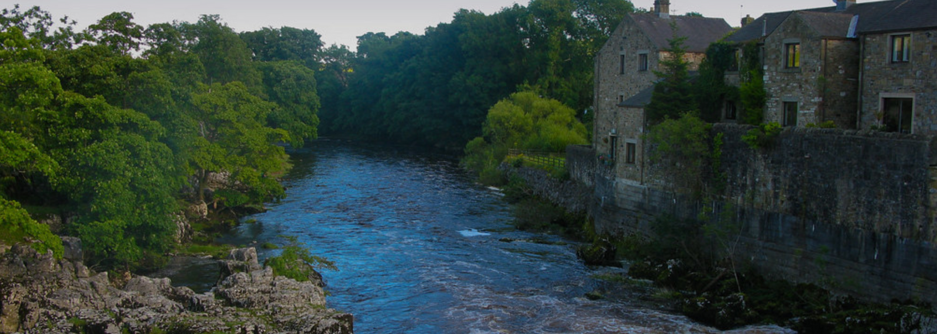 River flowing through a green landscape with stone buildings on the right side.