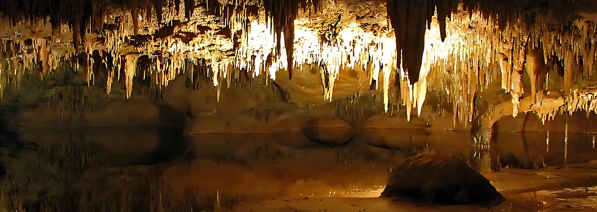 Cave interior with stalactites hanging from the ceiling and reflected in the water below.