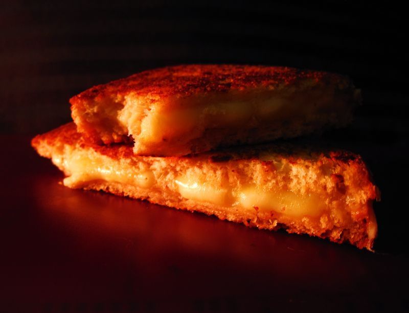 Grilled cheese sandwich, stacked, with melted cheese oozing out, golden-brown toasted bread.