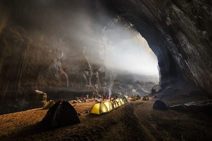 Tents glowing inside a vast cave, bathed in sunlight.