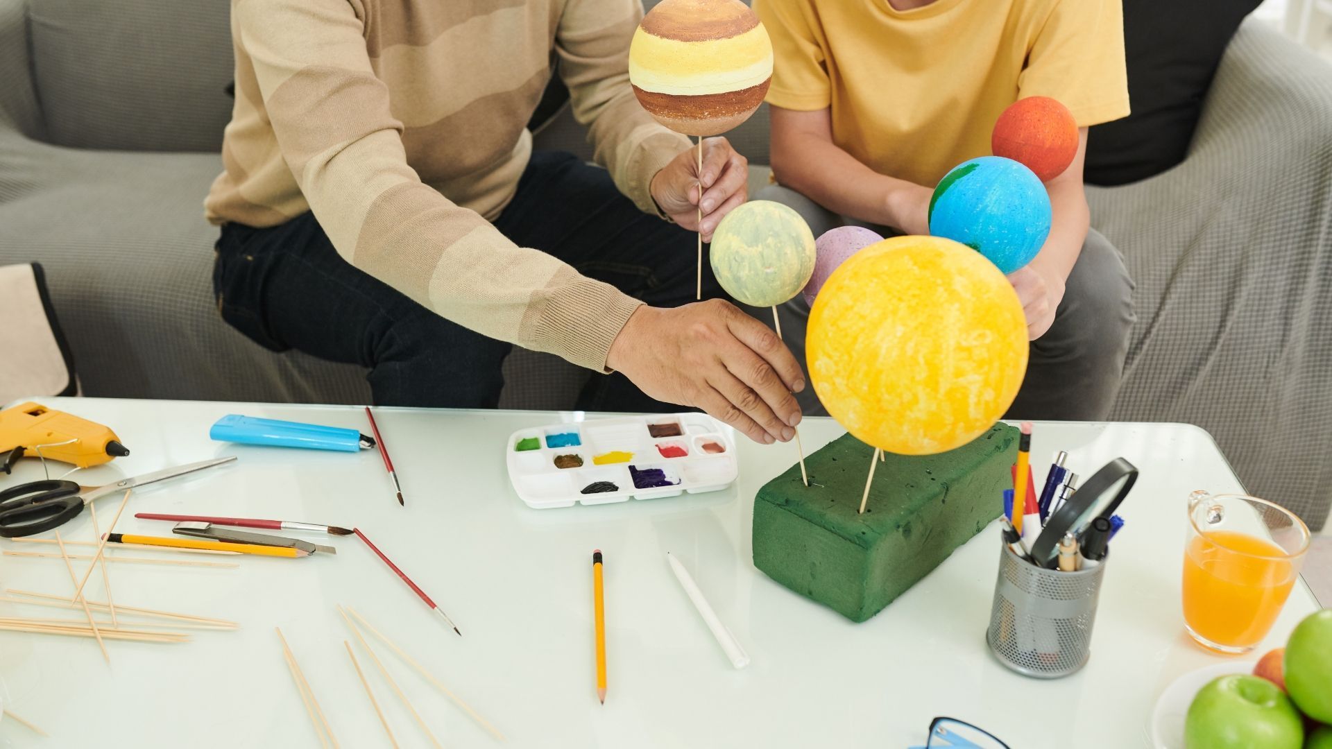Person assembling a solar system model with colorful spheres on sticks.