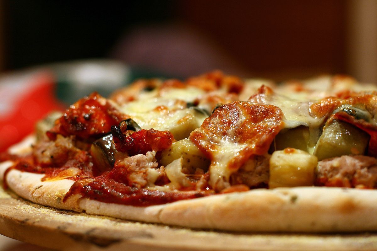Close-up of a pizza with cheese, pepperoni, and other toppings on a wooden board.