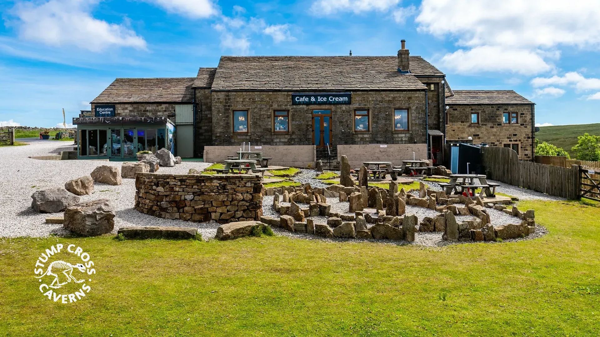 Stone building with outdoor seating area on a grassy lawn. The building features a sign that says, 
