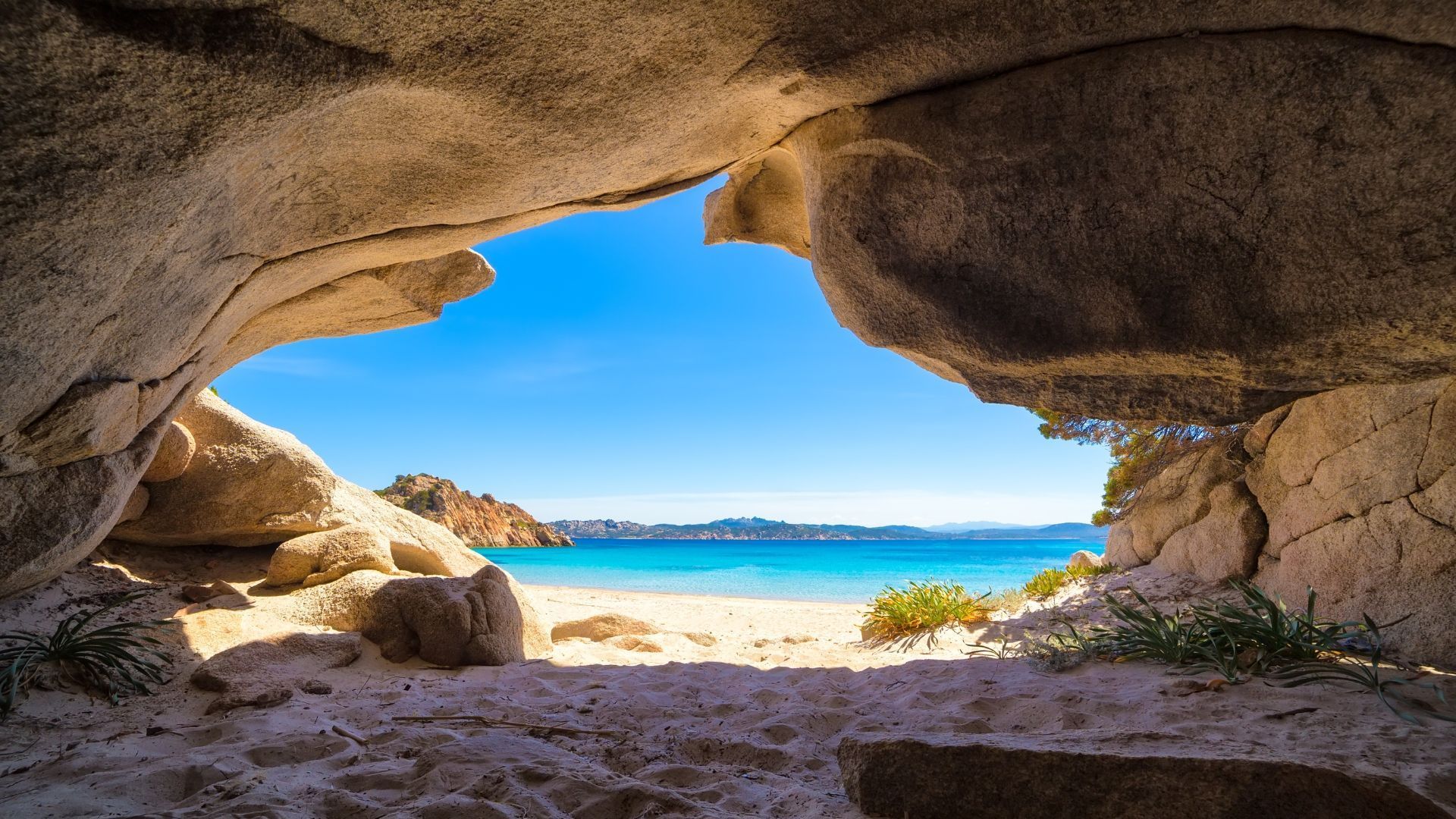Cave opening framing a view of a sandy beach, turquoise water, and blue sky.