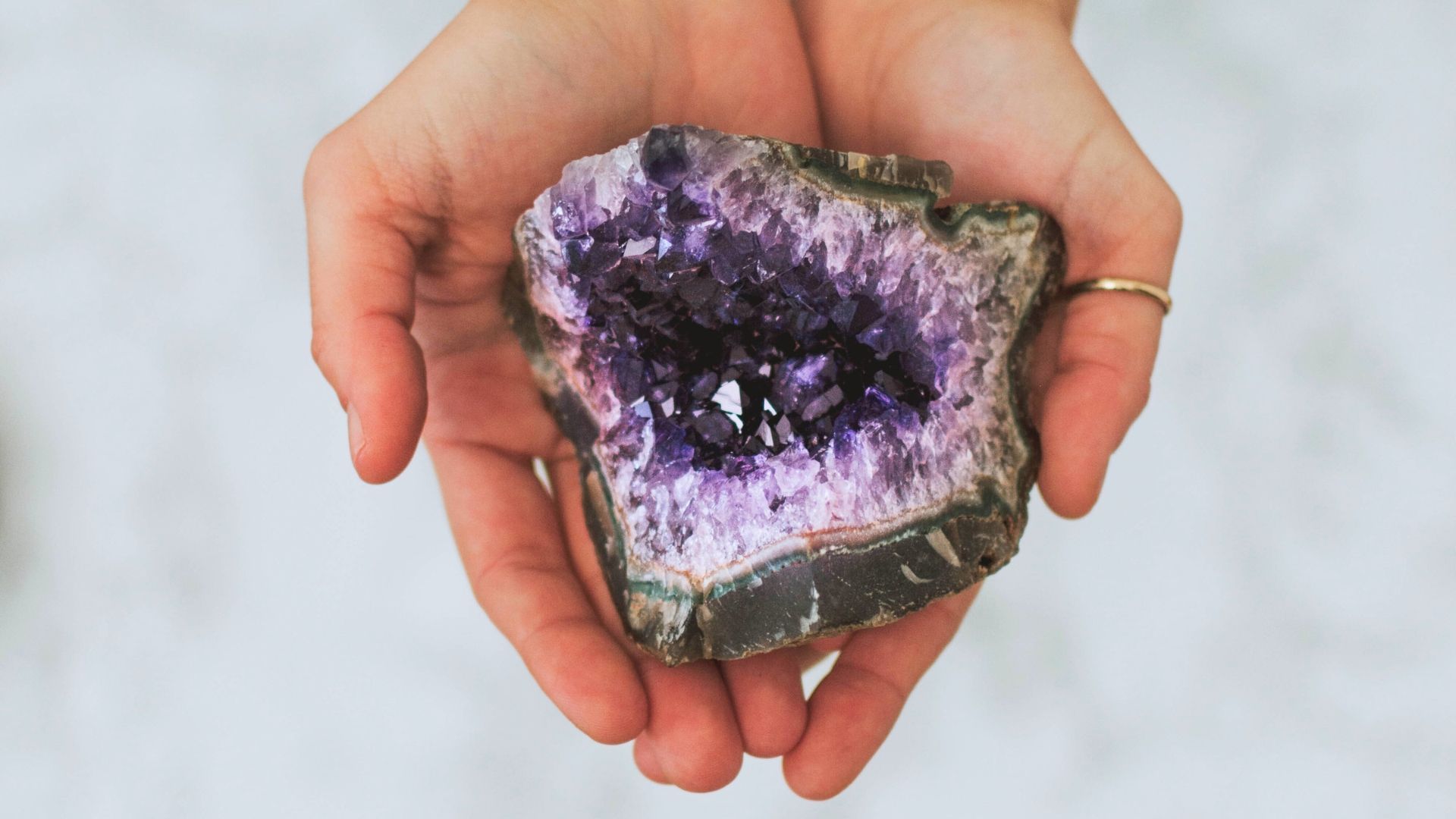 Hands holding a geode with purple crystals in the center.