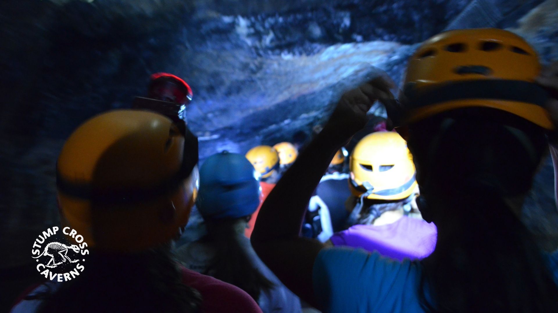 People in helmets exploring a dark cave, illuminated by headlamps.