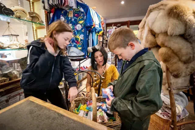 Two children and an adult looking at items in a shop, with a display of clothing and fur in the background.