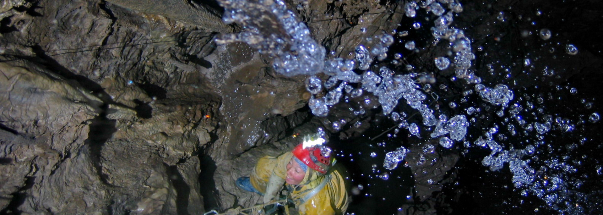 Water spraying in a dark cave, hitting colorful gear, likely a helmet, below.