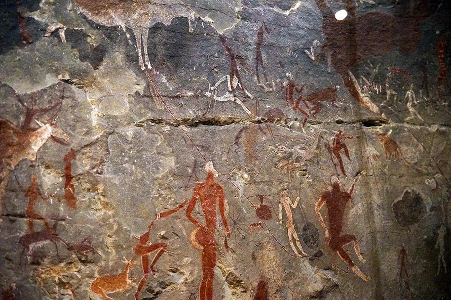 Cave painting depicting human figures and animals in red and white on a grey rock surface.