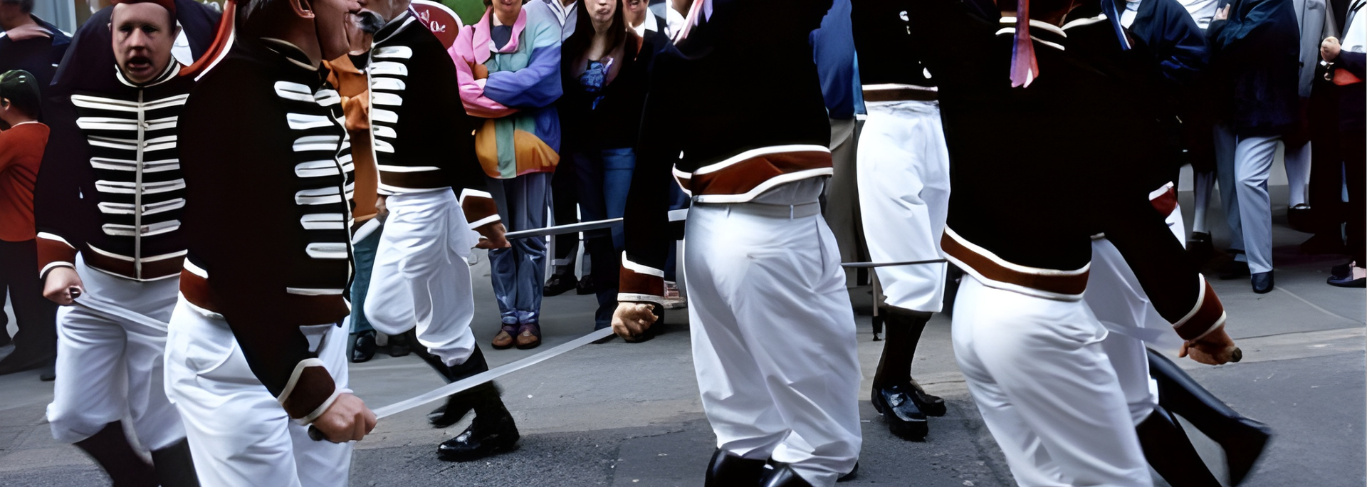 Men in uniform marching in a parade; white pants, black jackets, holding ropes. People watching.