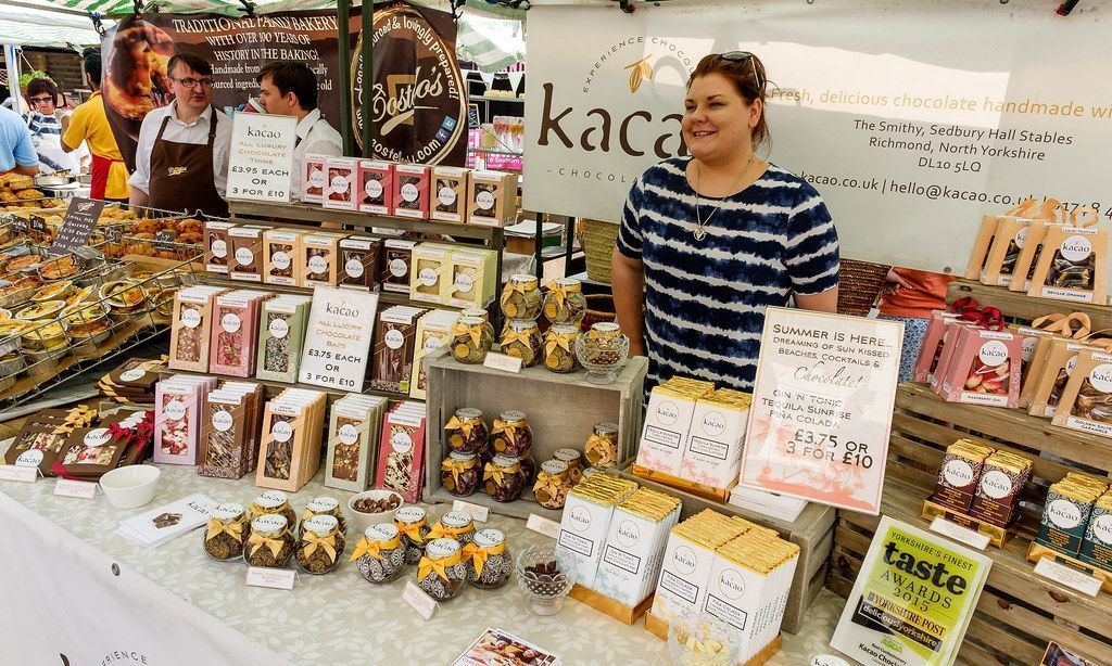 Woman at market stall with chocolate products for sale.