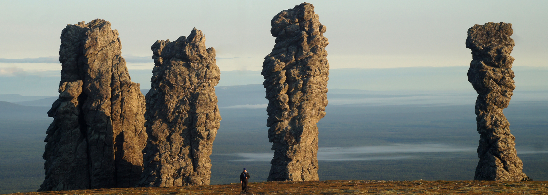 Tall, weathered rock formations on a plain. A person stands near the base of the formations.