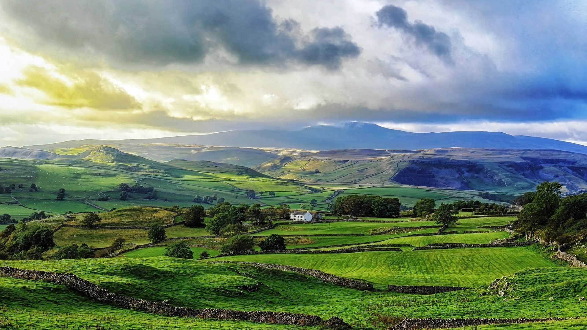 Rolling green hills under a cloudy sky, with mountains in the distance.