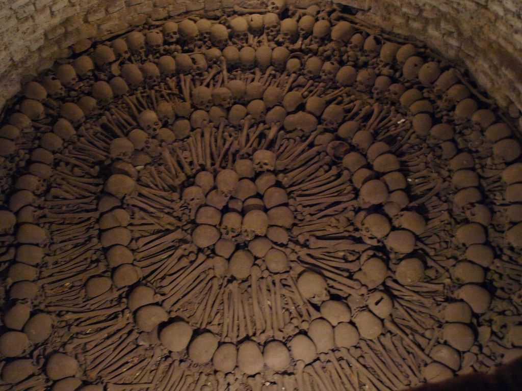 A dome-shaped chamber filled with many human skulls and bones arranged in concentric circles.