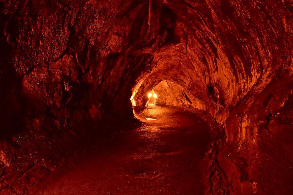 Lava cave interior illuminated by an unseen light source; red-orange rock walls and floor.
