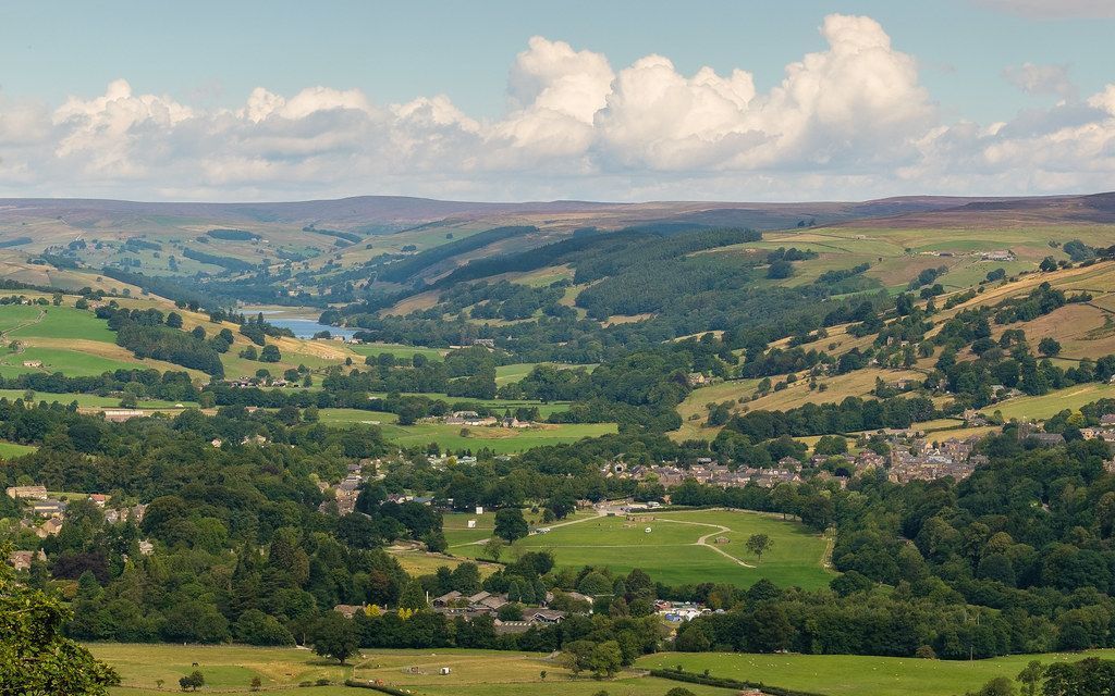 Rolling green hills, valleys, and scattered trees under a partly cloudy sky.