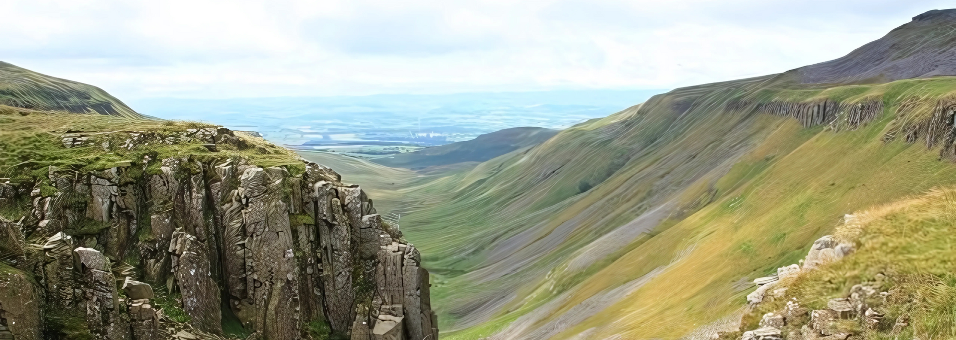 A deep green valley between two rocky mountains under a cloudy sky.