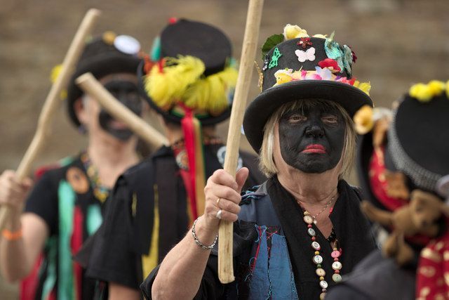 People in blackface, hats, and colorful outfits holding sticks, marching in a line.