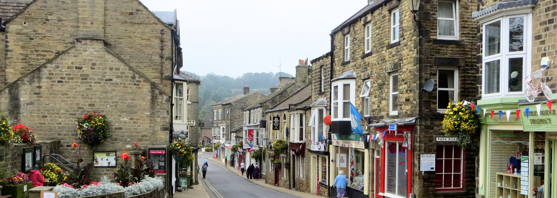 A narrow street in a historic town lined with stone buildings, shops, and hanging flower baskets.