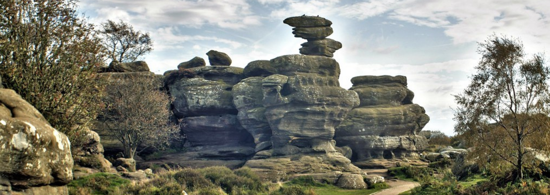 Rock formations in a landscape, with a path leading towards them under a cloudy sky.