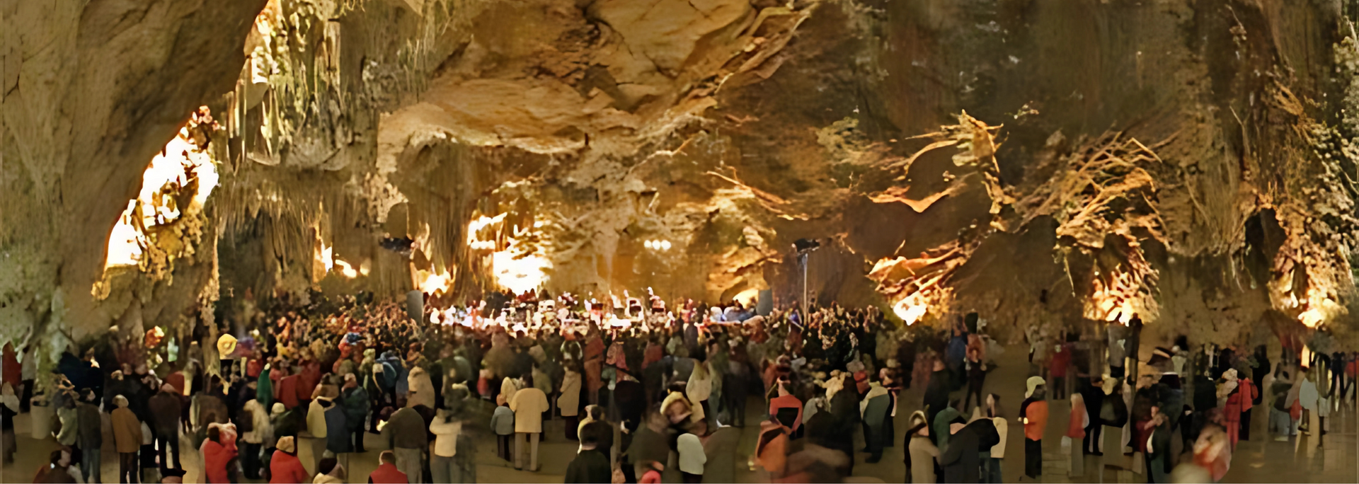 Large crowd of people gathered inside a cave, illuminated by lights.
