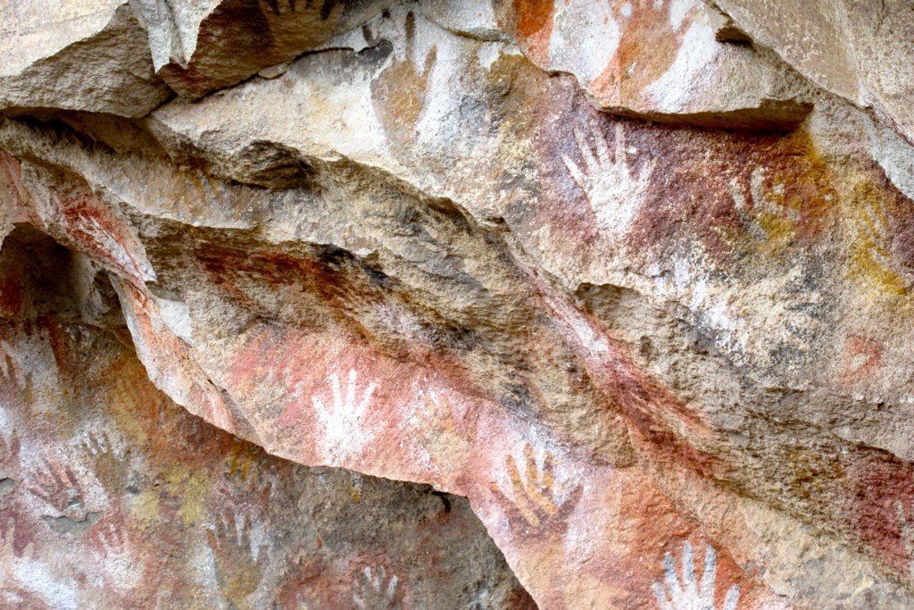 Handprints in red, white, and yellow ochre on a weathered rock face.