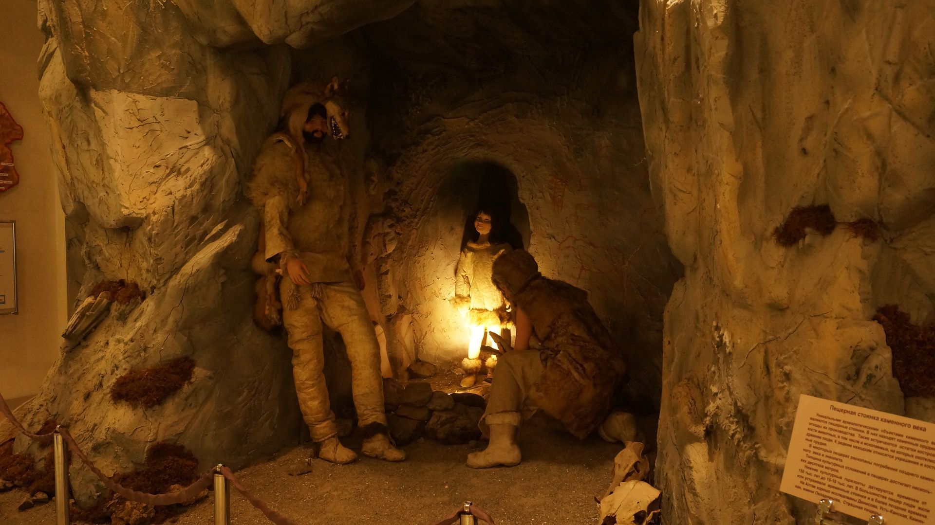 Cave diorama with three figures illuminated by a central light source. Two figures wear similar brown clothing.