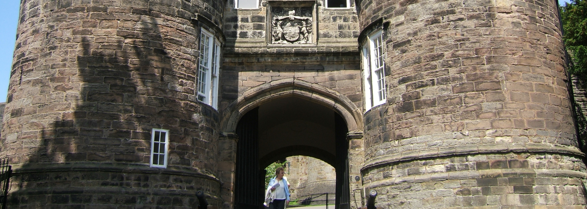 Stone archway entrance with two large round towers, a person stands in the archway.