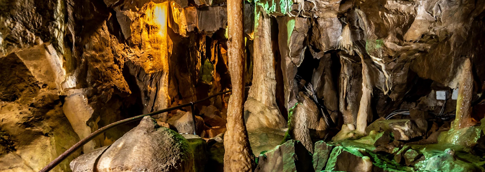 A cave interior with stalactites and stalagmites, lit with orange and green lights.