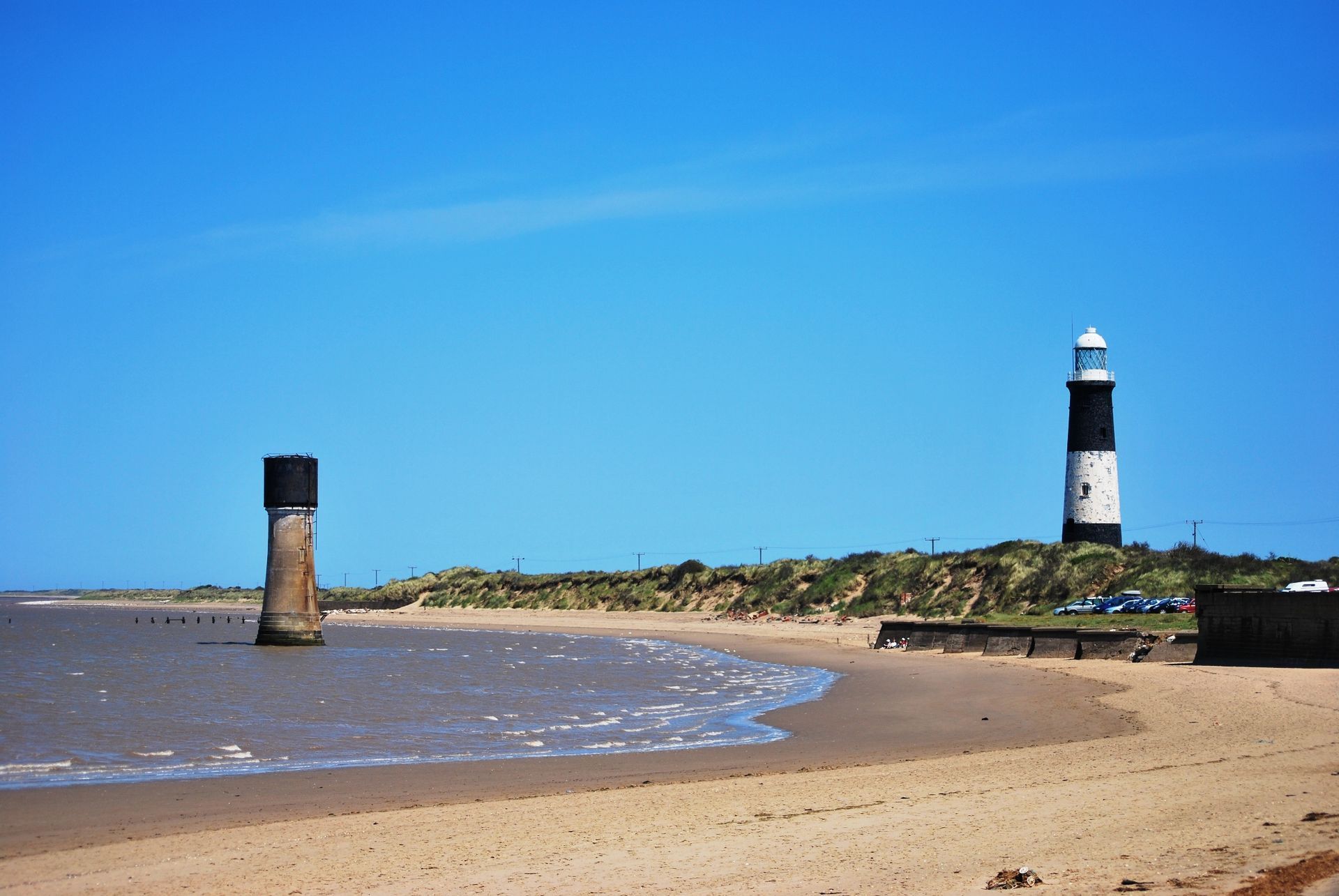 Beach with a black and white lighthouse under a clear blue sky.
