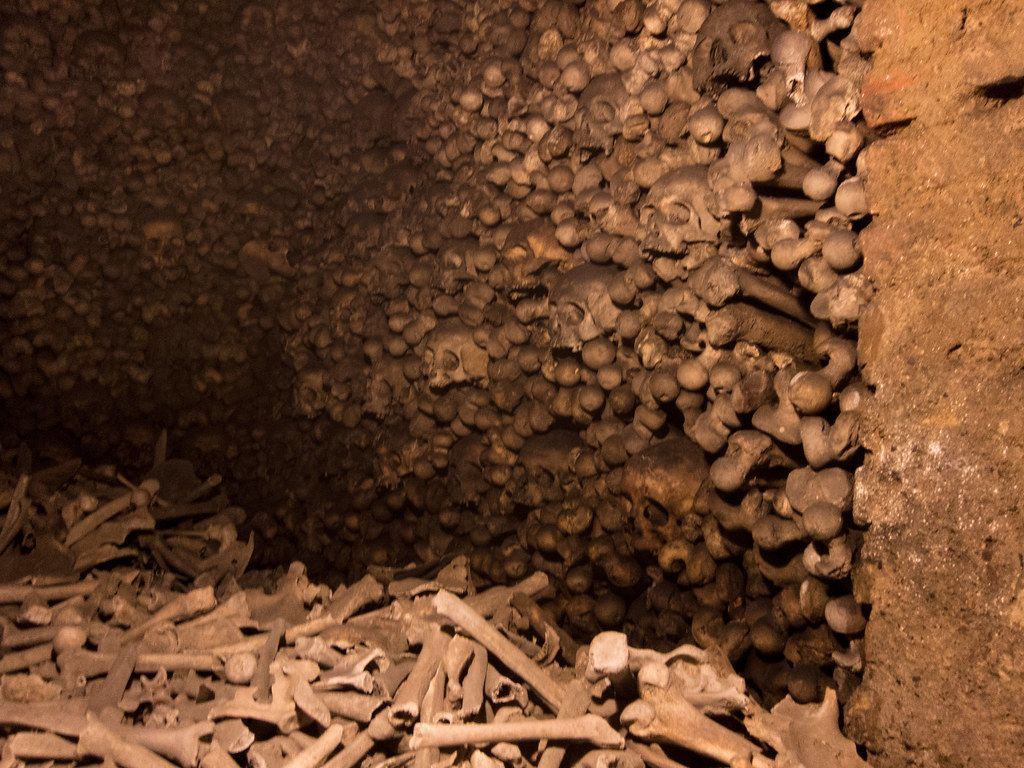 Bones and skulls stacked in a dark, underground cavern.